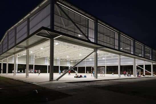 Pista polideportiva exterior iluminada por la noche con personas practicando deporte