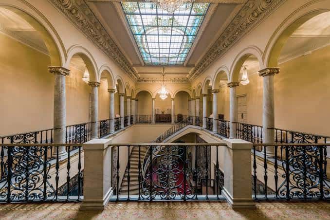 Gran escalera interior con cúpula de cristal y barandillas de hierro forjado