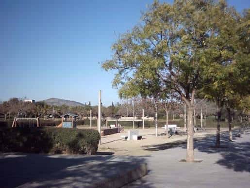 Vista general del parque con zona de juegos infantiles y árboles
