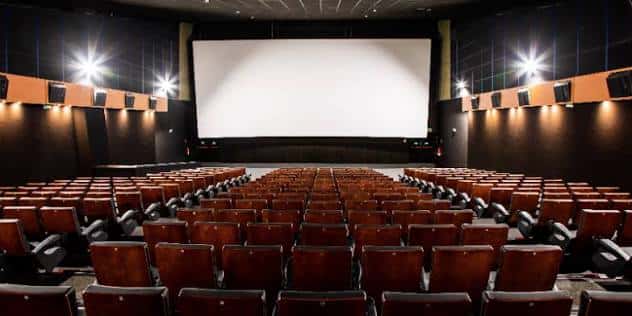 Sala de cine vacía con butacas de cuero marrón y gran pantalla blanca