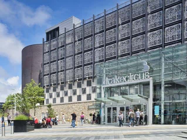 Entrada principal del centro comercial Drake Circus con letrero iluminado y fachada de cristal