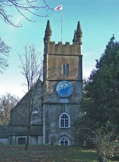 Vista exterior de la Stoke Damerel Church con su torre y reloj azul bajo un cielo despejado