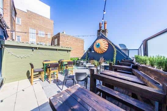 Terraza exterior del Oculist con mesas, sillas y decoración de luces en Brighton