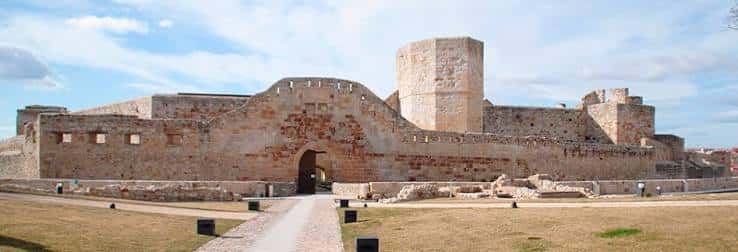 Fachada principal del castillo con torre cuadrada y entrada arqueada en día soleado