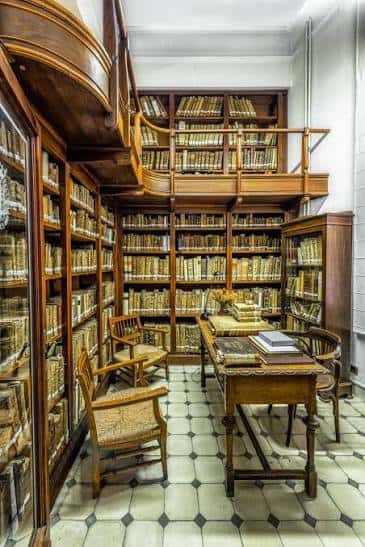 Sala de lectura histórica con estanterías de madera y mobiliario clásico