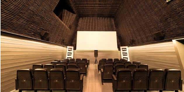 Interior del cine con butacas dispuestas frente a la pantalla y techo de madera texturizada