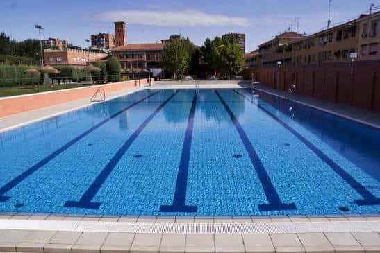 Piscina olímpica al aire libre con carriles marcados y entorno urbano al fondo