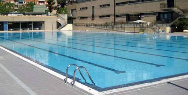 Piscina de competición con escaleras de acceso y edificio deportivo en el fondo