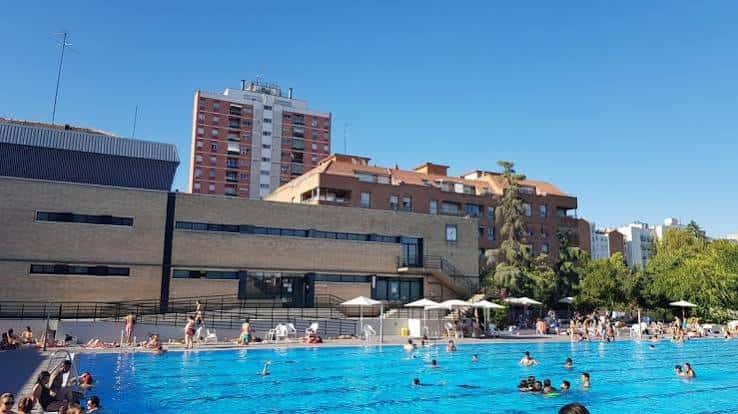 Piscina pública con usuarios disfrutando del agua y edificios residenciales al fondo