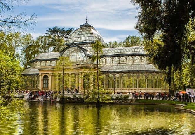 Vista del Palacio de Cristal rodeado de agua y árboles en el Parque del Retiro
