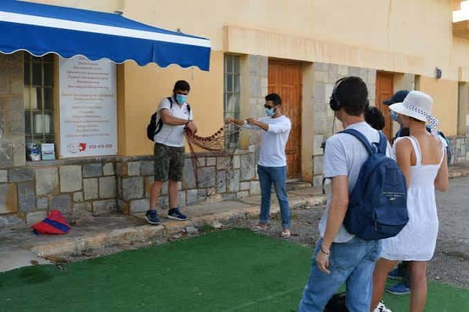 Grupo de visitantes en la lonja del pescado de Torrevieja, con un pescador mostrando una red