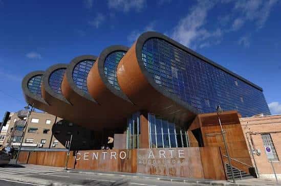 Fachada lateral del edificio con paneles de vidrio coloreado y la inscripción 'CENTRO DE ARTE ALCOBENDAS' en la base de madera