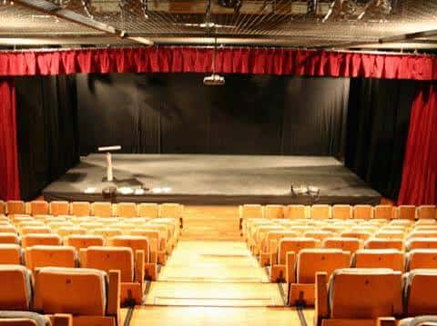 Interior del auditorio con escenario y butacas naranjas listas para evento