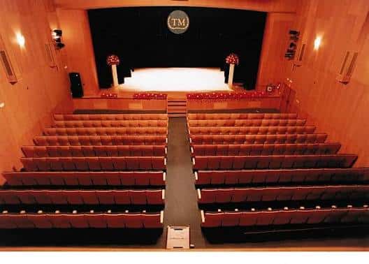 Interior del auditorio con butacas rojas y escenario iluminado