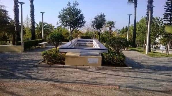Monumento o fuente central en el parque rodeado de vegetación y palmeras
