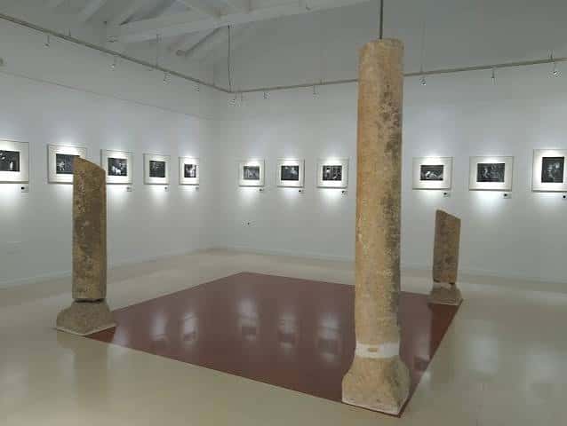 Interior de sala de exposiciones con columnas arqueológicas y fotografías enmarcadas en las paredes