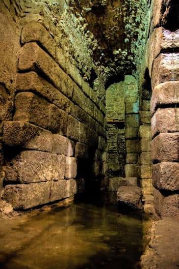 Interior de las Cuevas de Hércules con muros de piedra y agua en el suelo