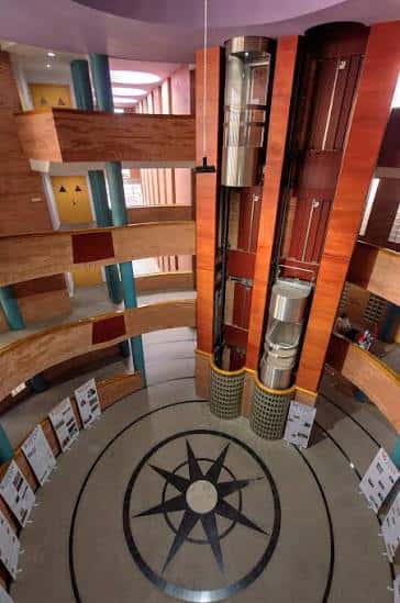 Vista cenital del atrio interior con escaleras curvas, ascensores de cristal y suelo decorado con rosa de los vientos