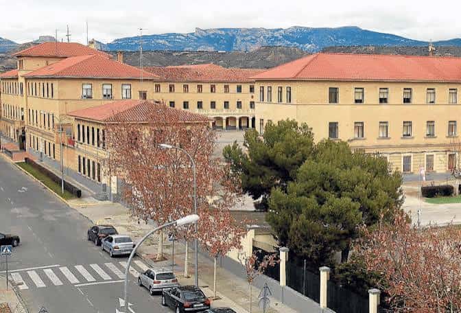 Fachada principal del Acuartelamiento Sancho Ramírez con montañas al fondo y árboles en primer plano