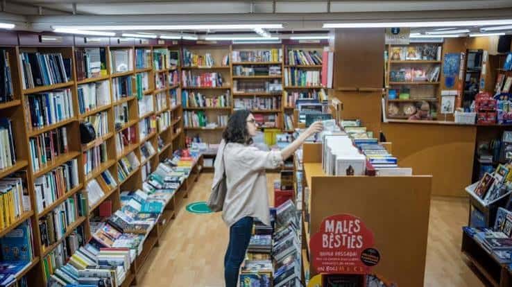 Interior acogedor de La Capona con estanterías llenas de libros y una cliente explorando