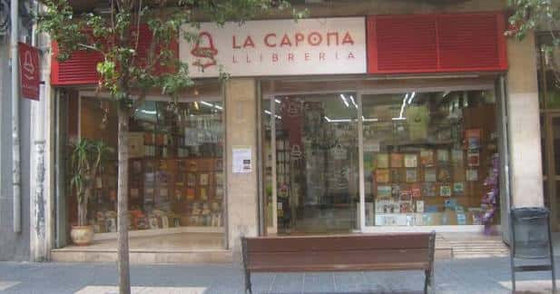 Fachada tranquila de La Capona con banco frente a la entrada y escaparate iluminado