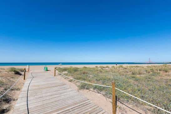 Pasarela de madera que conduce a la playa con mar y dunas en primer plano