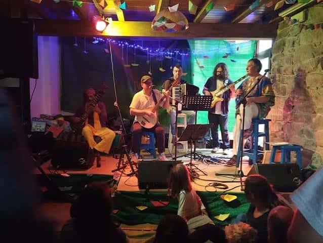 Bandas actuando en el escenario interior con iluminación colorida y público disfrutando del evento
