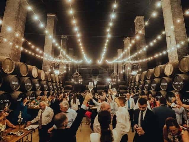 Interior de la bodega durante una celebración con invitados brindando bajo luces colgantes