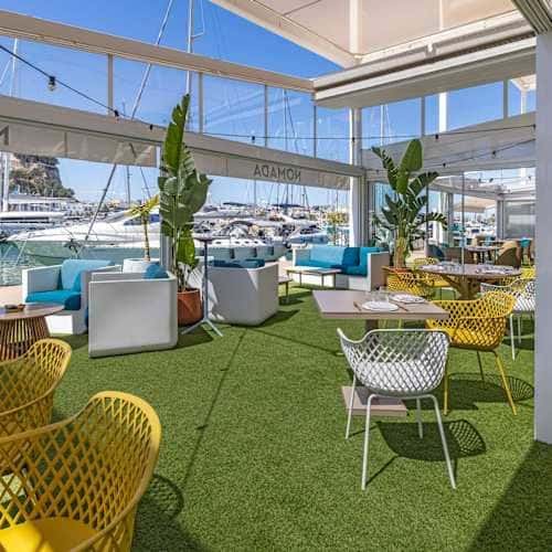 Terraza exterior del restaurante con césped artificial, mobiliario moderno y vista al puerto deportivo