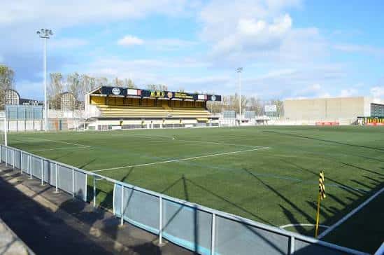 Vista general del campo de fútbol Baltasar Pujales con gradas amarillas y césped artificial bajo cielo parcialmente nublado