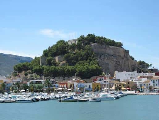 Castillo de Dénia dominando el puerto deportivo con embarcaciones y edificios costeros