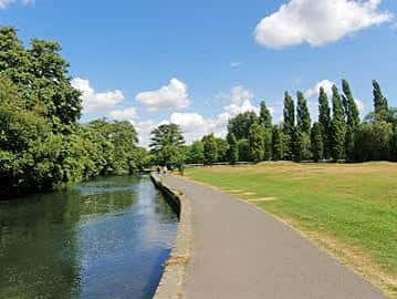 Paseo junto al río con césped y árboles bajo cielo azul