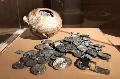 Exposición de monedas antiguas y un recipiente cerámico en vitrina del museo