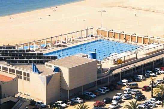 Perspectiva elevada del Centre Natació Mataró junto a la playa, mostrando instalaciones y aparcamiento