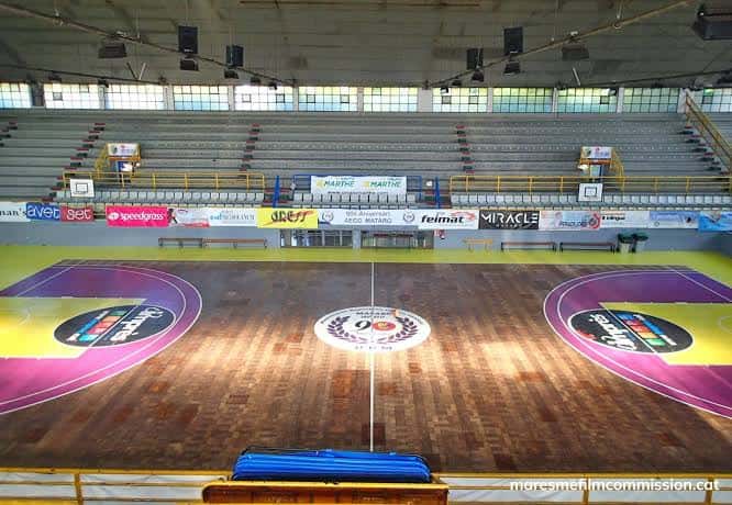 Plano cenital de la cancha de baloncesto con logotipo central y publicidad en las gradas