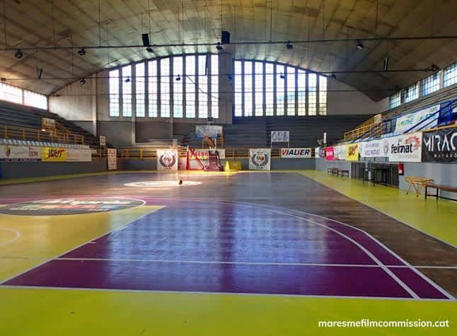 Vista lateral de la pista de baloncesto con gradas y grandes ventanales en el fondo