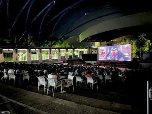 Escenario del auditorio con pantalla gigante y público sentado en mesas durante la noche