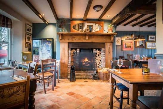 Interior acogedor de The Fox and Roman con chimenea encendida y decoración rústica