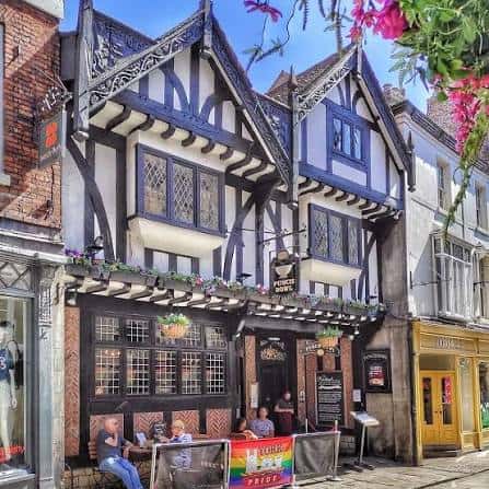 Fachada histórica del pub The Punch Bowl con arquitectura Tudor y clientes en terraza