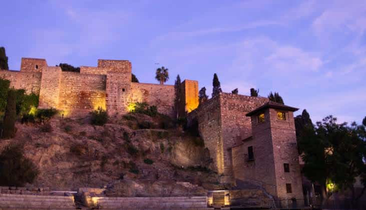 Alcazaba iluminada al atardecer con tonos cálidos en las paredes y cielo violeta