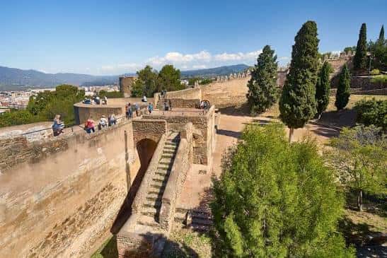 Vista panorámica de las murallas del Castillo de Gibralfaro con visitantes y la ciudad de Málaga al fondo