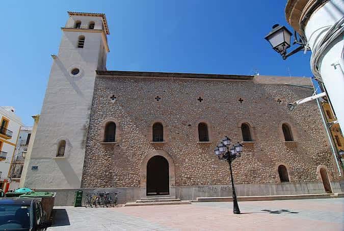 Vista lateral de la iglesia mostrando mampostería y campanario bajo cielo azul