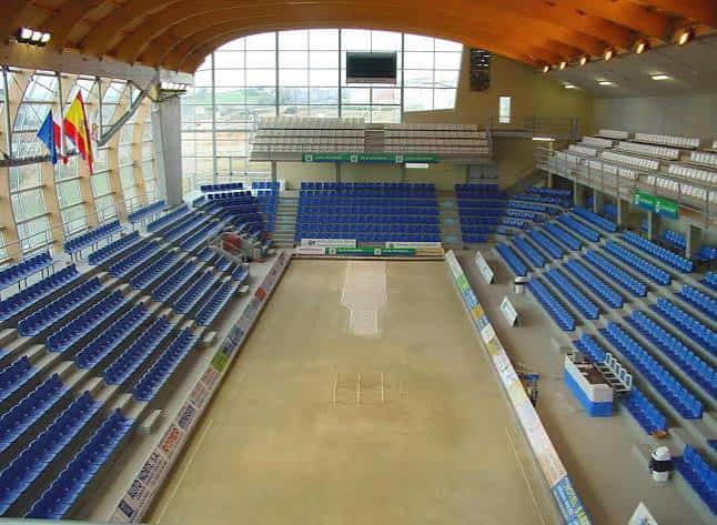 Interior de la bolera con pista de juego, gradas azules y techo de madera