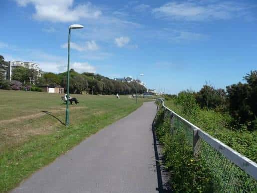 Sendero peatonal en West Cliff Gardens con césped y árboles bajo cielo azul