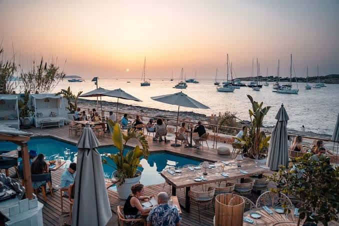 Vista panorámica del restaurante Monkey Ibiza al atardecer con el mar y veleros al fondo