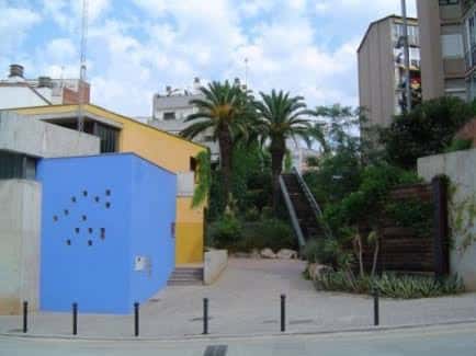 Fachada exterior del local social con paredes azules y amarillas, rodeado de vegetación y palmeras