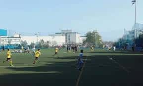 Campo de fútbol del complejo con jugadores en actividad y estructura deportiva al fondo