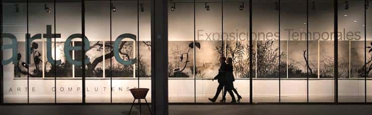 Fachada de cristal del Centro de Arte Complutense con siluetas de visitantes