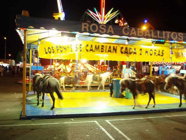 Vista nocturna de un carrusel de ponis iluminado en el recinto ferial