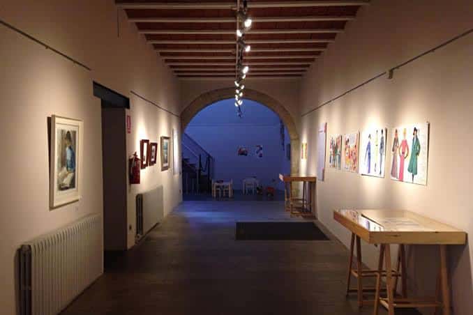 Vista interior del Espai Expositiu Aula Cultural mostrando el pasillo principal con obras expuestas y arcos de piedra